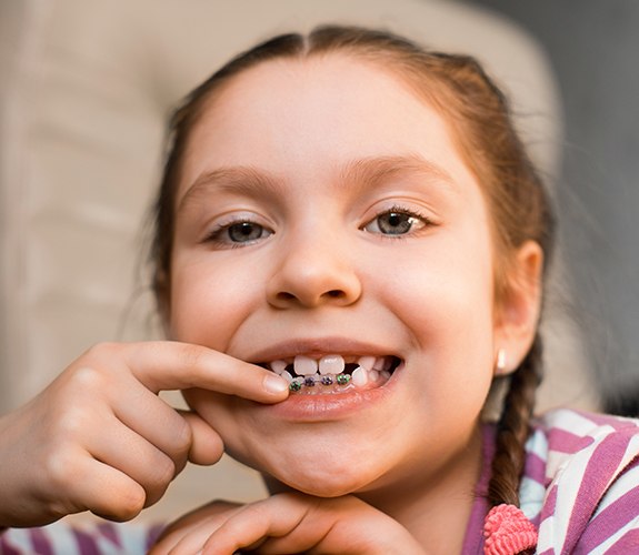 Child pointing to her smile with phase one pediatric orthodontics