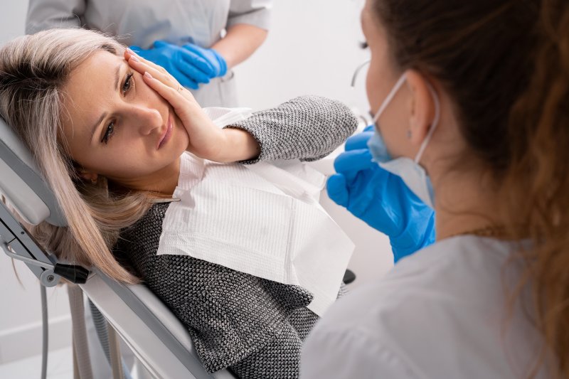 a female patient experiencing dental pain and holding her cheek